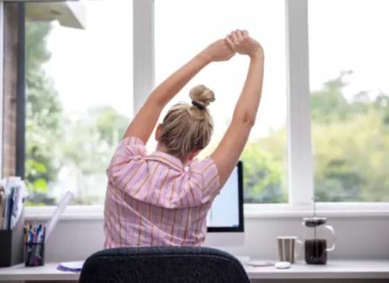 woman-sitting-in-office-chair-stretching-at-office-desk