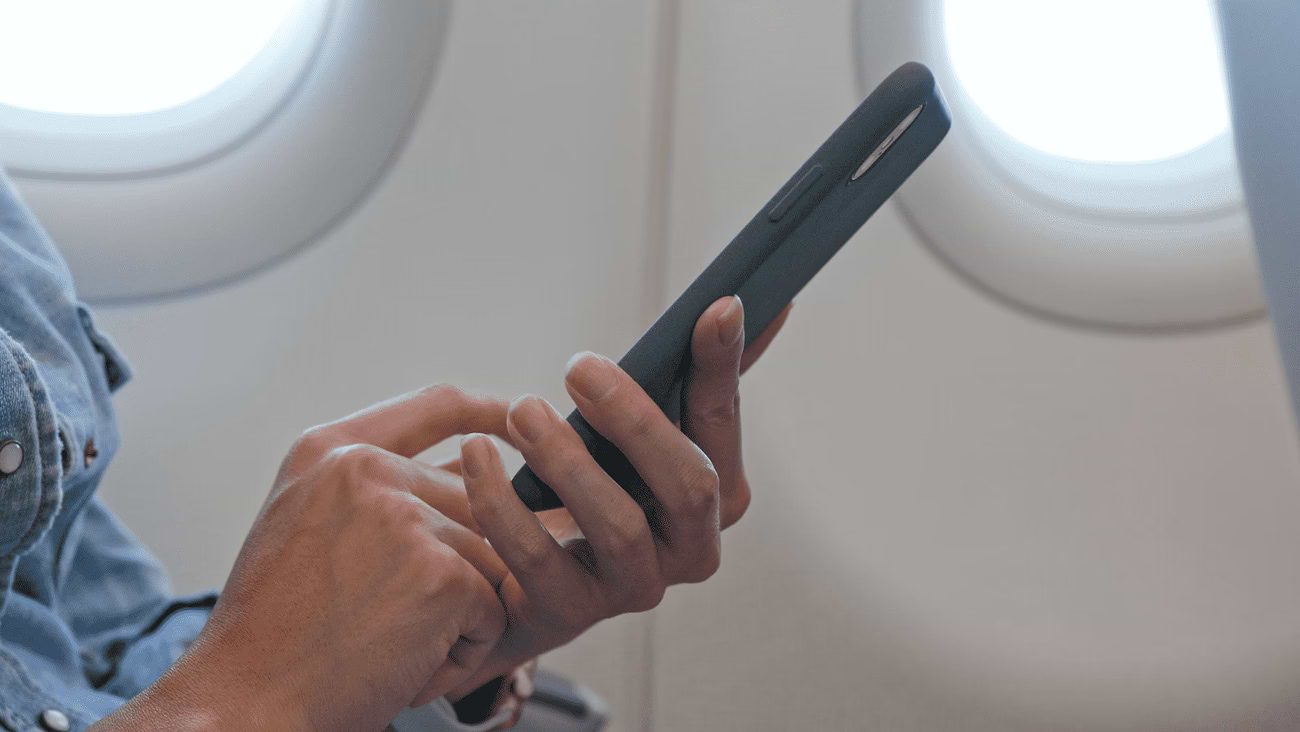 A man on a plane is surfing on his phone after comparing the prices of surfing packages