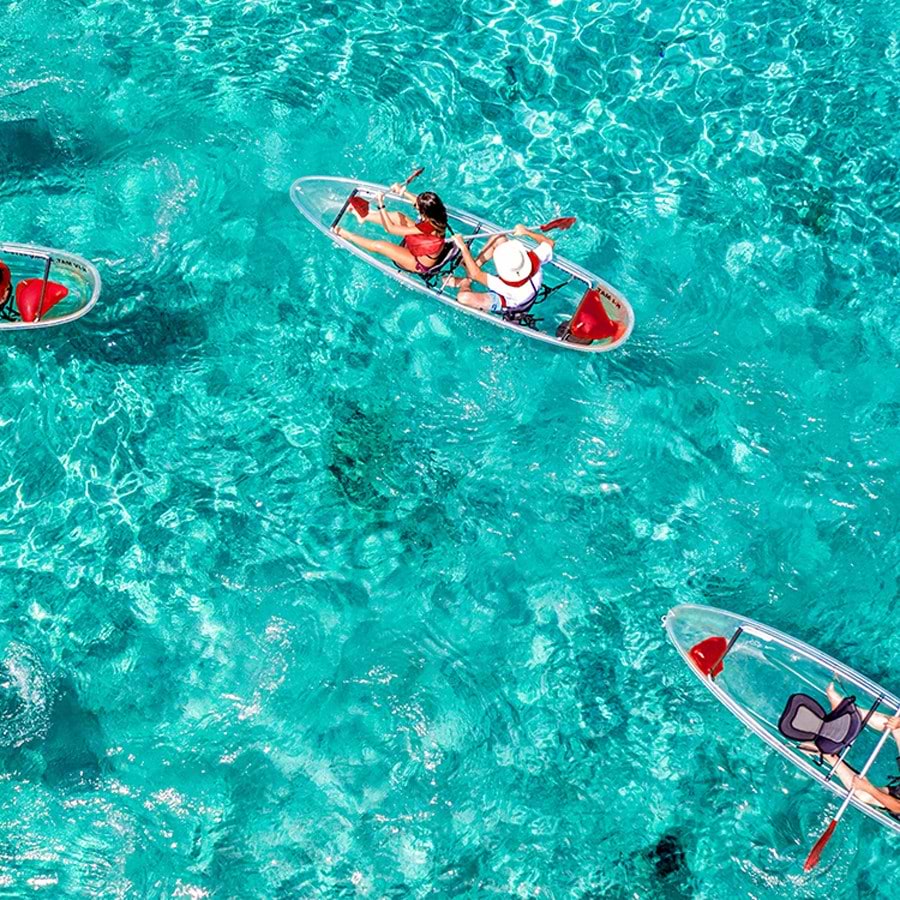 A group of people on tandem kayaks with clear bottoms paddling through turquoise waters