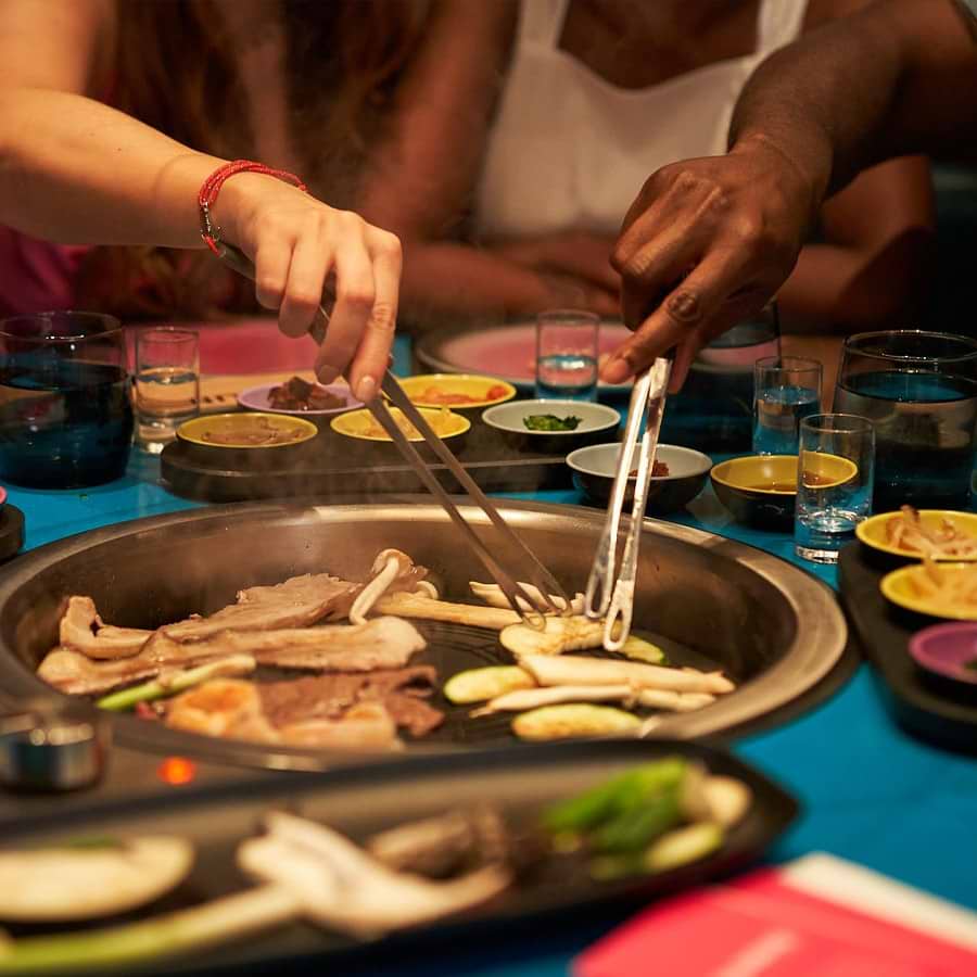 Hands holding tongs cooking various items at their dining table