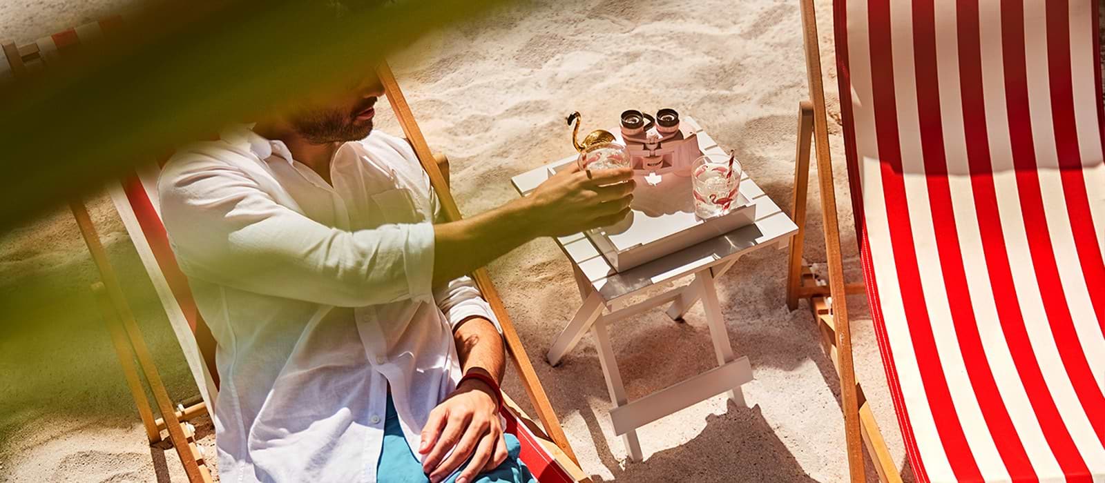 A man holding a beverage while seated on a beach lounger